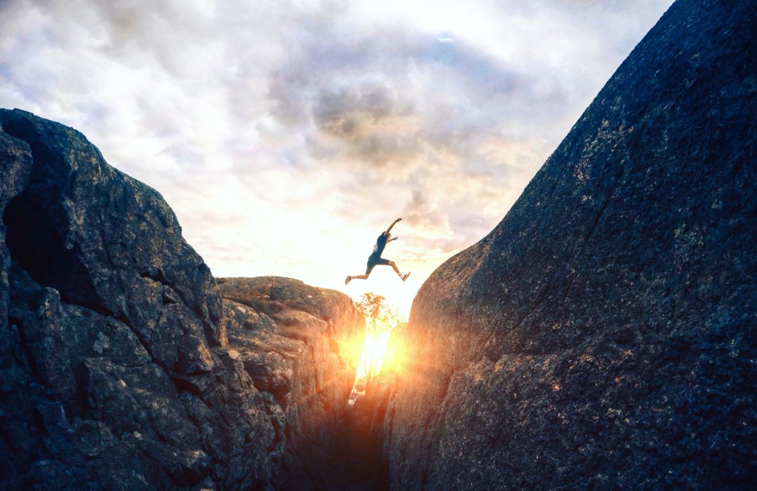 Person jumping between rocky cliffs at sunrise